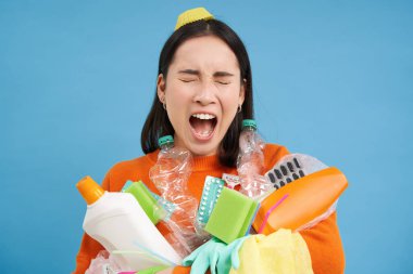 Ağlayan üzgün kızın plastik çöplerle portresi, geri dönüşüm atıkları topluyor, sefil görünüyor, mavi arka plan.