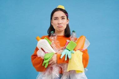 Yüzünde çöp olan karmaşık bir kız. Plastik boş şişeler ve atıklar. Sorunlu ve üzgün görünüyor..