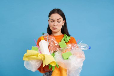 Doğayı önemsemek. Plastik şişe ve atık taşıyan genç bir kadın. Gönüllüler çöpleri toplayıp geri dönüşüme götürdüler. mavi izole arkaplan.