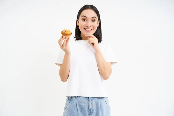 stock image Bakery and sweets. Happy asian woman looking at tasty cupcake, eating pastry, white background.