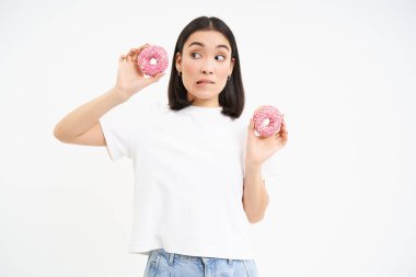 Asyalı bir kızın elinde diyetini bozmayı düşünen iki çörek var. Donutlara şüpheyle bakıyor..