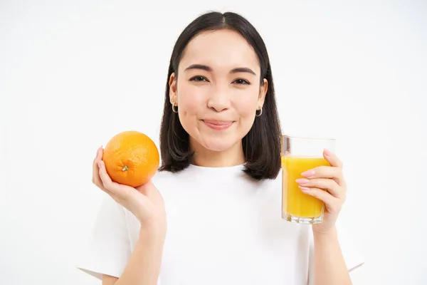 stock image Close up portrait of brunette girl, 25 years, holding fresh glass of juice and orange fruit, smiling, eats healthy food, white background.