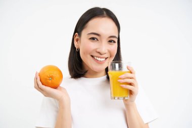 Sağlıklı, gülümseyen Koreli bir kız, portakaldan sıkılmış taze meyve suyu içiyor, sağlıklı kalıyor, normal besleniyor, beyaz bir geçmişi var..