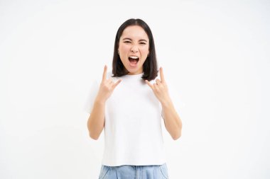 Heyecanlı Asyalı kadın, rock 'n' roll yapıyor, heavy metal kornaları çalıyor, eğleniyor, konser veya festivalin tadını çıkarıyor, beyaz arka plan.