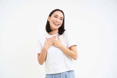 Samimi, gülümseyen Asyalı kadın portresi, gülüyor ve gülümsüyor, beyaz arka plan üzerinde t-shirt ve kot ile poz veriyor.