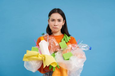 Üzgün kız geri dönüşüm yapmak zorunda. Elinde plastik şişeler ve çöp var. Sıkıntılı ve sinirli görünüyor..