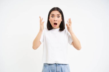 Şok olmuş ve korkmuş Asyalı kadın, soluk soluğa kalmış ve endişeli görünüyor, beyaz arka planda izole edilmiş. Boşluğu kopyala