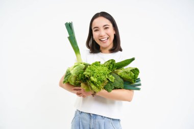 Gülümseyen Asyalı kadın görüntüsü, bir sürü yeşil sebzeli vejetaryen, orantısız yiyecekler yiyen, beyaz arka planda izole edilmiş..