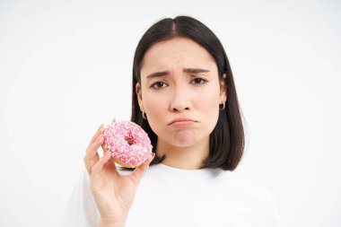 Üzgün, hıçkıra hıçkıra ağlayan kız abur cubur yiyemez, lezzetli jöleli donut gösterir, ısırmak ister, beyaz arka plan.