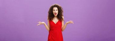 Woman being shocked guy breaking up with her during party. Concerned pissed and outraged good-looking lady in red dress with evening makeup shrugging with spread palms in clueless and questioned pose.
