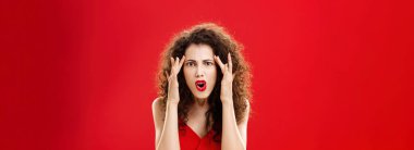 Woman cannot understand how dumb person should be. Pissed and annoyed displeased angry woman with curly hairstyle in red dress holding fingers on temples complaining on stupid people around her.
