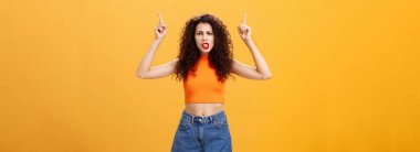 Kıvırcık saç stili olan hoşnutsuz bayan müşterinin kapalı çekimleri. kırmızı ruj serinletilmiş üst kısmı, kafa karıştırıcı ve tatminsiz bir ifadeyle portakal rengi üzerinden açıklama talep ediyor.