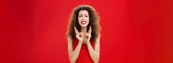 不安定な希望に満ちた女性 赤い口紅の巻き毛で歯を食いしばって歯を食いしばるのは幸運を祈るために指を横断する — ストック写真