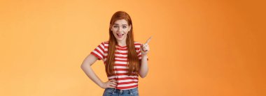 Canlı kızıl saçlı kadın sol üst köşeyi işaret eden, gülümseyen, neşeyle konuşan, el ele tutuşan, rahat poz veren, turuncu arka plan neşeli reklam veren yeni trend hakkında konuşuyor..