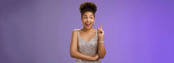 stock image Creative joyful dreamy young african-american girl in silver dress raise index finger eureka gesture look aside inspired have awesome idea sharing suggestion tell plan aloud, standing blue background.