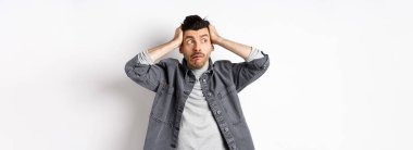 Paniğe kapılmış bir adam, paniğe kapılmış ve paniğe kapılmış bir şekilde logoya bakıyor, sorun yaşıyor, el ele tutuşuyor, beyaz arka planda duruyor..