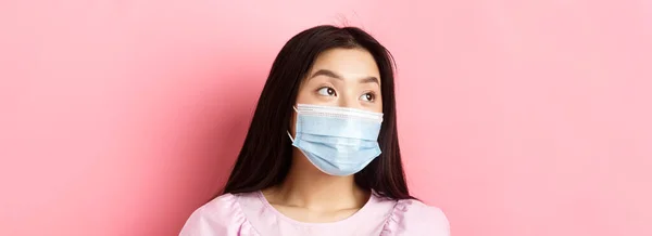 Covid パンデミックおよび検疫の概念 医療マスクで夢のアジアの女の子のクローズアップは 思慮深い顔でロゴを見て ピンクの背景に立って — ストック写真