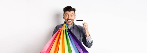 Ευτυχισμένος Τύπος Shopaholic Κρατώντας Πολύχρωμες Τσάντες Ψώνια Και Δείχνει Πλαστική — Φωτογραφία Αρχείου