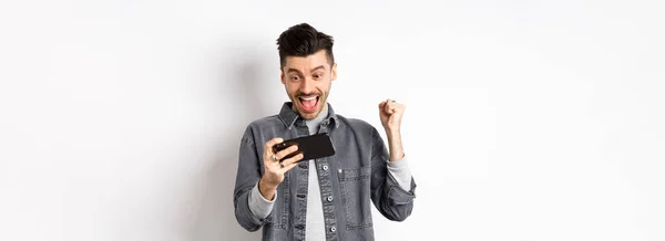 快乐的男人大喊 在手机上赢了电子游戏 胜利了 实现了在线目标 站在白底上 — 图库照片