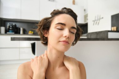 Ev sporları ve refah. Spor giyimli genç esmer kadın, evde kalıyor ve yoga yapıyor, dikkatli egzersizler yapıyor, yoga pozunda oturuyor gözleri kapalı ve rahat bir yüzle. Boşluğu kopyala