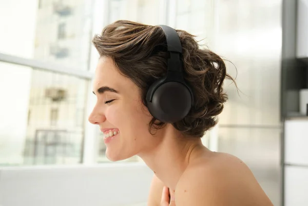 Close up portrait of young smiling woman, fitness girl in headphones, listens music and does workout training at home, exercise indoors, practice yoga and pilates.