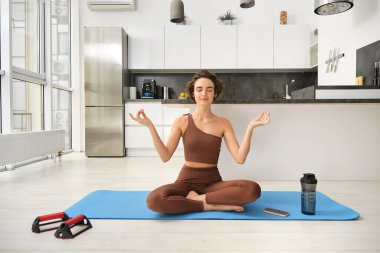 Gülümseyen kız atlet, spor kadın aktif giyimde yoga yapıyor, nilüfer pozisyonunda yoga minderinde oturuyor, meditasyon yapıyor, farkındalık egzersizleri yapıyor..