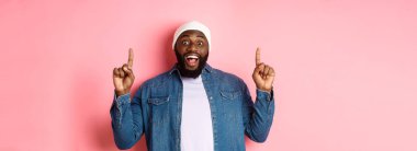Neşeli siyahi adam harika bir reklam sunuyor, parmaklarını havaya kaldırıyor ve gülümsüyor, pembe arka planda duruyor..