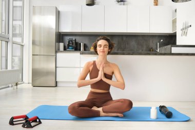 Gülümseyen kız atlet, spor kadın aktif giyimde yoga yapıyor, nilüfer pozisyonunda yoga minderinde oturuyor, meditasyon yapıyor, farkındalık egzersizleri yapıyor..