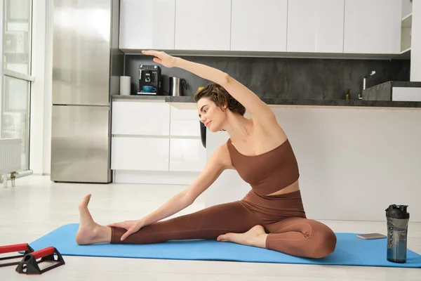 Image of young beautiful woman stretching her arms, workout at home on rubber yoga mat, practice fitness indoors.