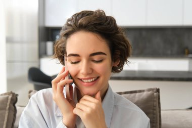 Gülümseyen güzel bir kadının yakın portresi, cep telefonuyla konuşmak, akıllı telefonla sohbet etmek, birini aramak, evde oturmak..