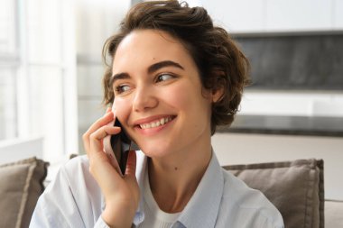 Gülümseyen güzel bir kadının yakın portresi, cep telefonuyla konuşmak, akıllı telefonla sohbet etmek, birini aramak, evde oturmak..