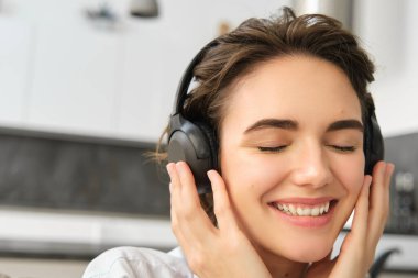 Güzel bir genç kadının yakın portresi, kablosuz kulaklıkla gülümseyen ve müzik dinleyen, iyi ses kalitesinin tadını çıkaran..