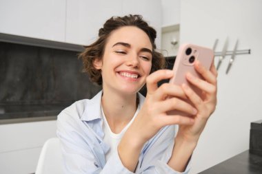 Cep telefonundaki esmer kadın sohbetlerinin portresi, evden akıllı telefon uygulaması, mutfakta otururken siparişler..
