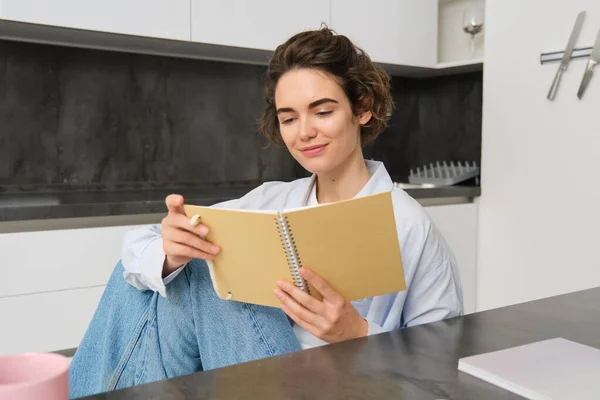 stock image Image of brunette girl reading through her notes, writing in journal, studying while sitting at home.