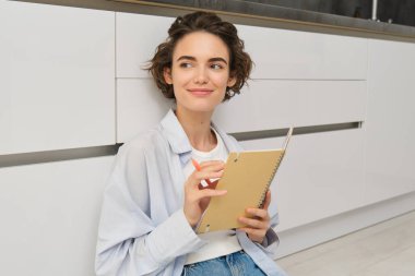 Şirin esmer kadının portresi yere oturur, ajandasını çizer, mutfakta yere günlük yazar ve gülümser. Boş zaman, yaşam tarzı ve insan konsepti