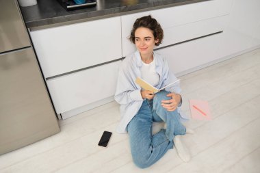 Kız öğrencinin evde çalışmasının en iyi bakış açısı. Genç bir kadın elinde günlükle yerde oturuyor, ajandasına bir şeyler yazıyor, defterde notlar okuyor..