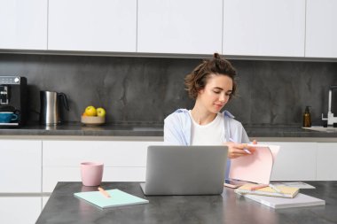 Evde çalışan kadının portresi, defterini kontrol ediyor, sayfayı çeviriyor, dizüstü bilgisayarla online toplantıya bağlanıyor. Kız programlamayı uzaktan öğreniyor, internet eğitimi alıyor..