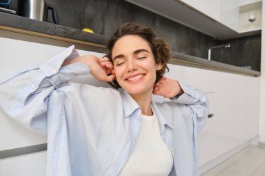 Memnun, çekici genç bir kadın, elleri kapalı ve mutlu bir gülümsemeyle uzanıyor, mutfakta yerde oturuyor..