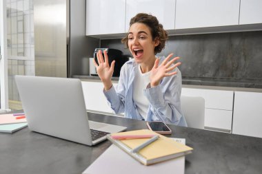 Dost canlısı, güler yüzlü bir kadın evde oturuyor, dizüstü bilgisayara el sallıyor, merhaba diyor, online toplantıya katılıyor, görüntülü sohbete bağlanıyor..