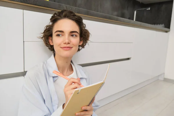 stock image Close up portrait of young woman writing in her journal, feeling creative, sitting with planner, notebook and pen on floor, studying, doing her homework at home.