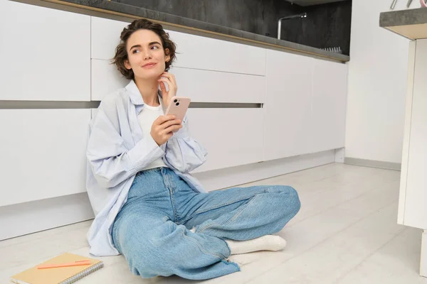 stock image Portrait of girl with mobile phone, sits on floor at home, orders takeaway in app. Young woman with smartphone does online shopping from home, browsing websites.