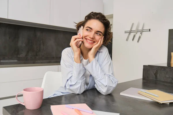 Stock image Portrait of young woman, 25 years old, holding smartphone, talking on mobile phone, sitting in kitchen at home.