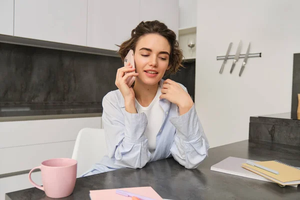 stock image Portrait of young woman, 25 years old, holding smartphone, talking on mobile phone, sitting in kitchen at home.