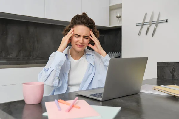 女人在家工作时头疼 女孩有痛苦的偏头痛 坐在笔记本电脑旁 因不适而面带微笑 — 图库照片