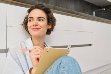 Yaratıcı, gülümseyen genç bir kadının yakın portresi, elinde kalemle yerde oturuyor, günlüğe yazıyor, notlar alıyor, ödevlerini yapıyor, ajandasına notlar yazıyor..