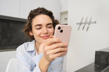 Evde oturup cep telefonunu kontrol eden mutlu bir gülümsemeyle akıllı telefona bakan bir kadının portresi..