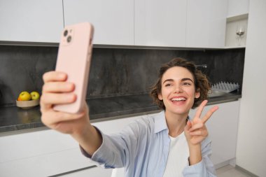 Mutlu, güzel esmer kız evde selfie çekiyor, akıllı telefonuyla poz veriyor..