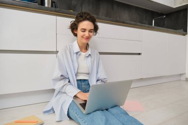 Genç bir IT kızı, kadın evden bağımsız çalışıyor, dizüstü bilgisayarla yerde oturuyor. Kız öğrenci internette ödev yapıyor, bilgisayar klavyesine yazıyor..