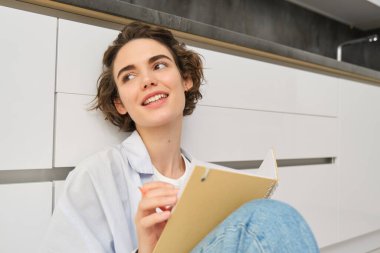 Hobiler ve yaşam tarzı konsepti. Mutlu genç bir kadın elinde kalem ve defterle yerde oturuyor. Günlüğüne wirtes, günlüğüne notlar alıyor. Programını planlayıp kağıda çiziyor..