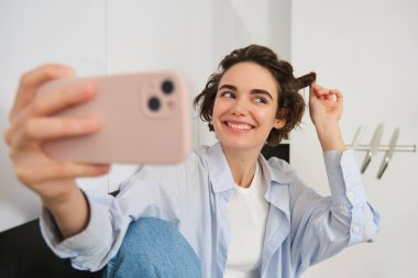 Güzel esmer kadının portresi, selfie çekiyor ve bukleleriyle oynuyor, cep telefonu uygulamasında fotoğraf çekiyor ve gülümsüyor..